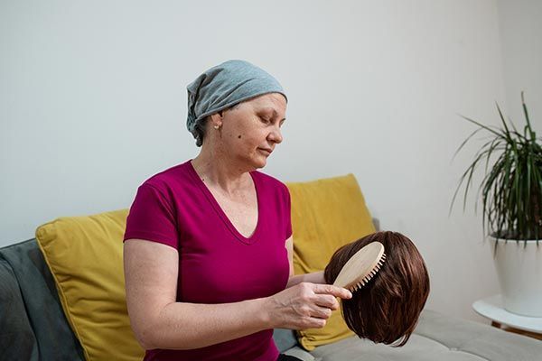 A woman with cancer is brushing her wig with a brush.