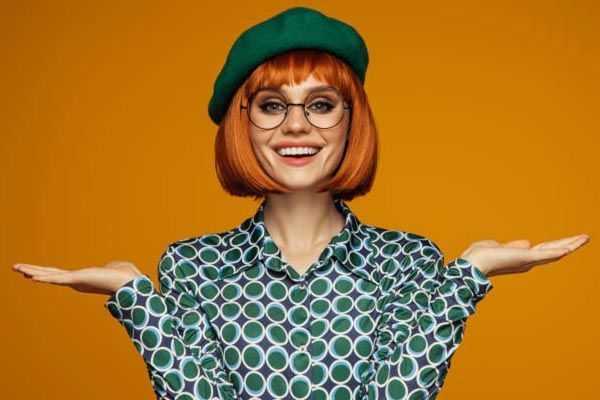 A woman with red hair and glasses is wearing a green beret and a green shirt.