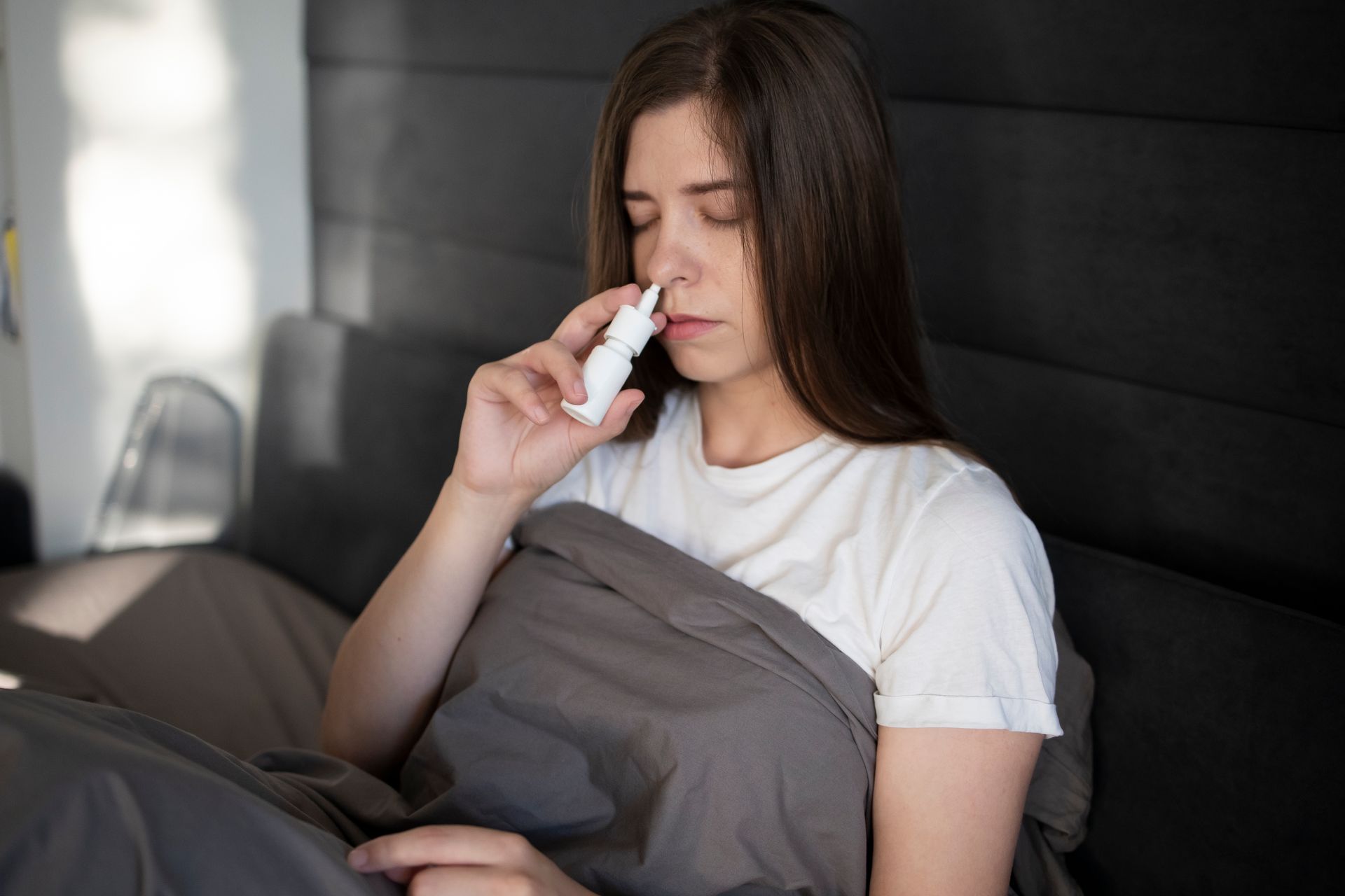 A woman with nasal congestion spraying decongestant medication