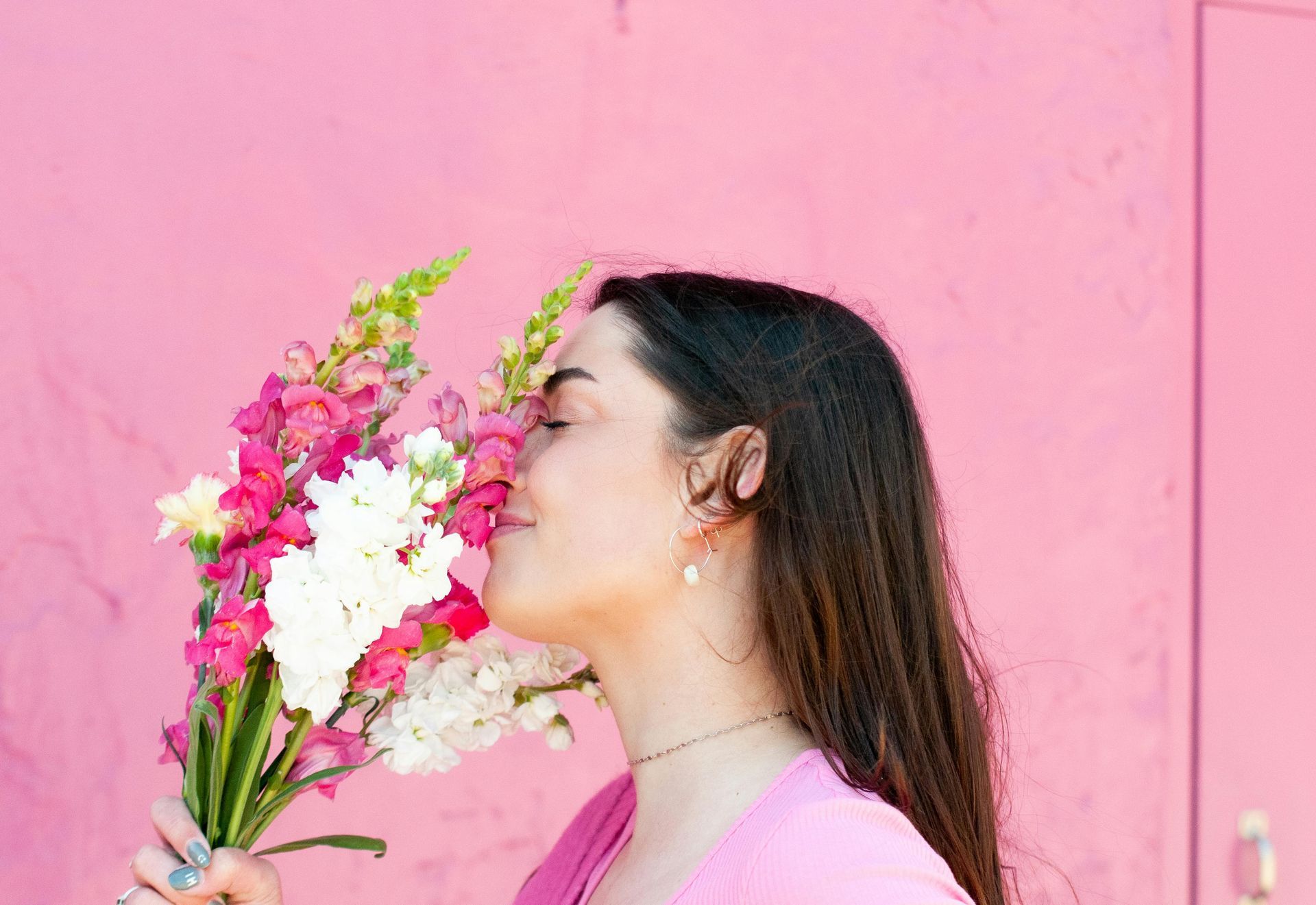 A woman is smelling a bouquet of flowers in front of a pink wall.