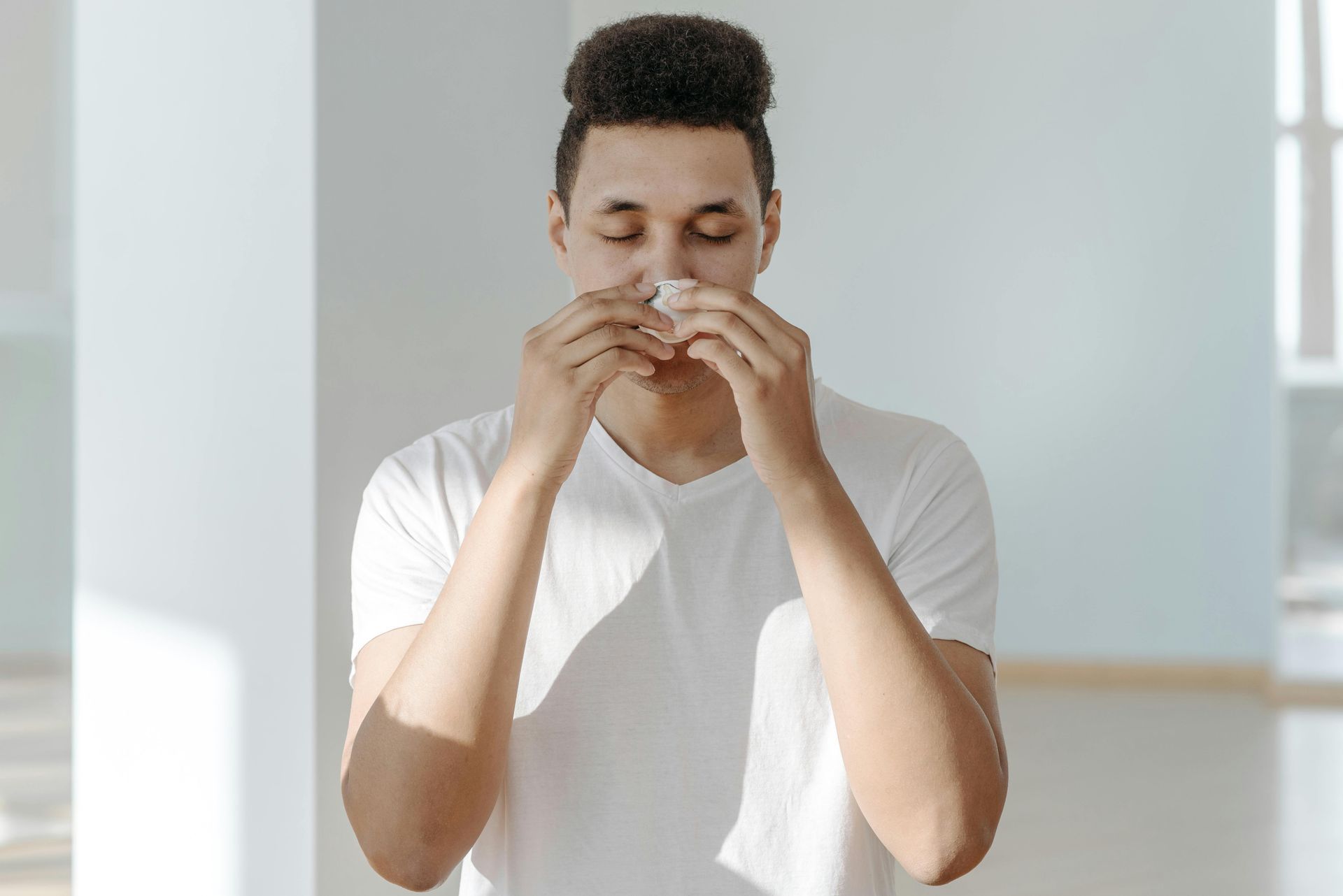 A man in a white shirt is blowing his nose with a napkin.