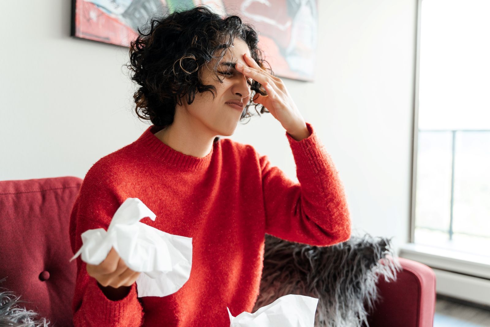 Person suffering from sinus infection, holding tissue touching their face, likely due to a cold.