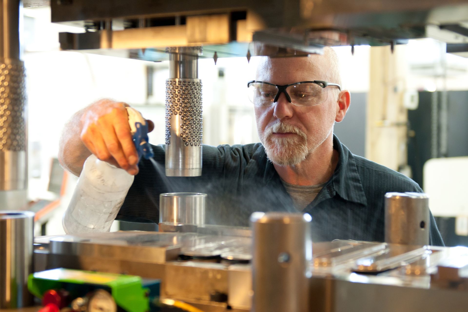 A man wearing glasses is working on a machine in a factory.