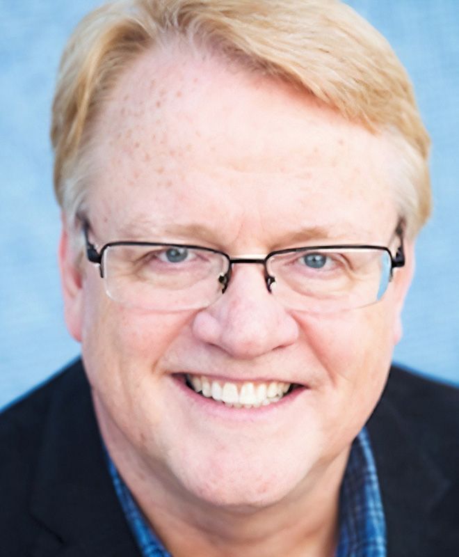 A man (Doug Thorpe) wearing glasses is smiling for the camera