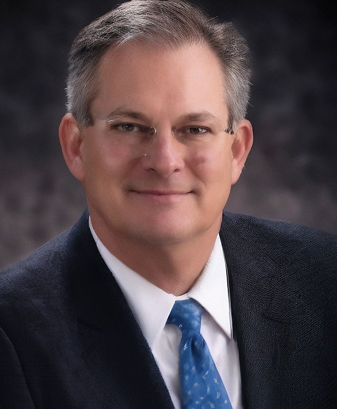 A man (Gerald Merfish) in a suit and tie is smiling for the camera