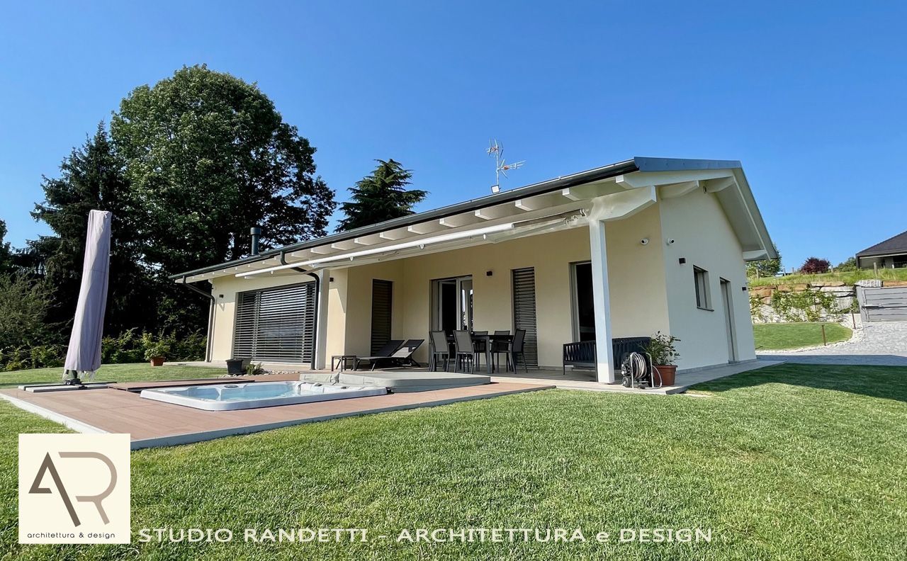 Casa moderna a un solo piano, di colore bianco, con patio coperto, prato e cielo azzurro, in un contesto suburbano.