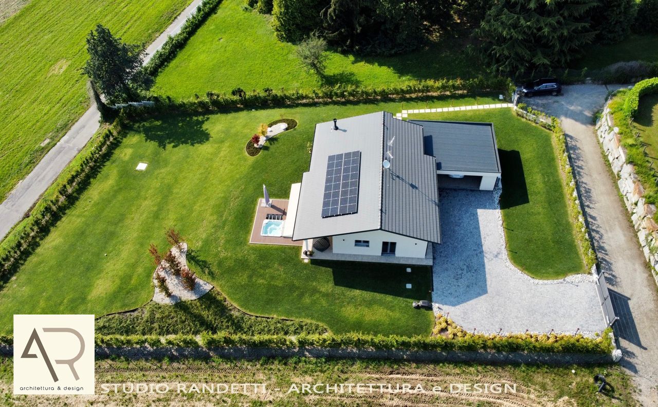 Veduta aerea di una casa moderna con pannelli solari, circondata da un vialetto di ghiaia e un prato verde.