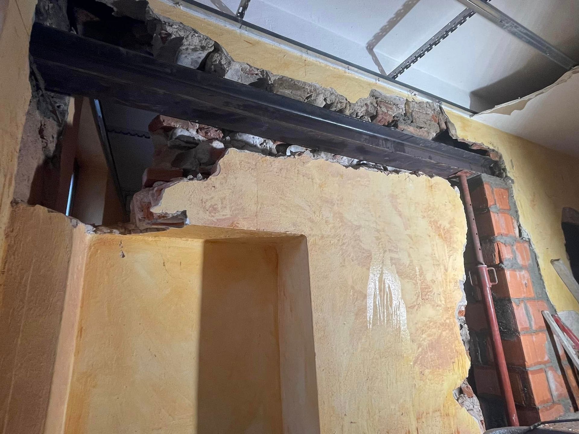 In una stanza, soffitto e pareti danneggiati con mattoni a vista, trave annerita e intonaco scrostato.