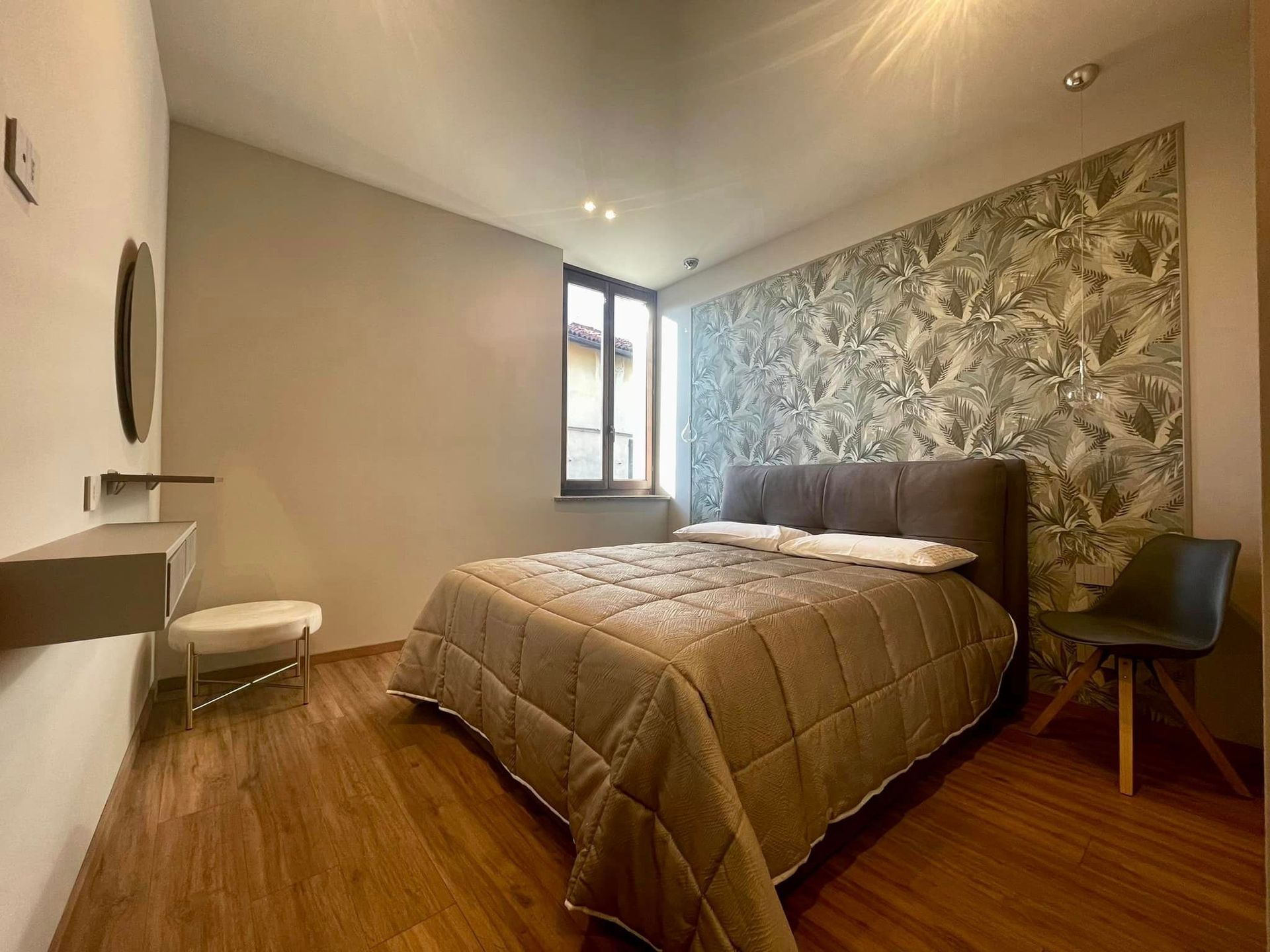 Camera da letto moderna con letto, parete decorativa con motivo, pavimento in legno e finestra con luce naturale.