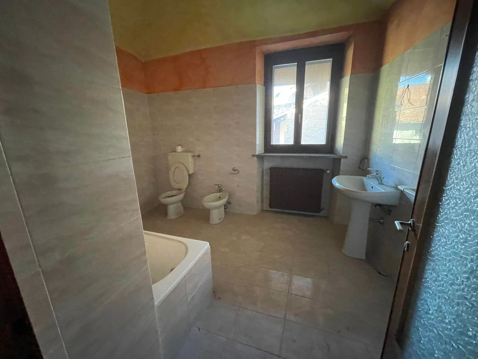 Piccolo bagno con vasca, WC, lavandino e finestra, illuminato da luce naturale.