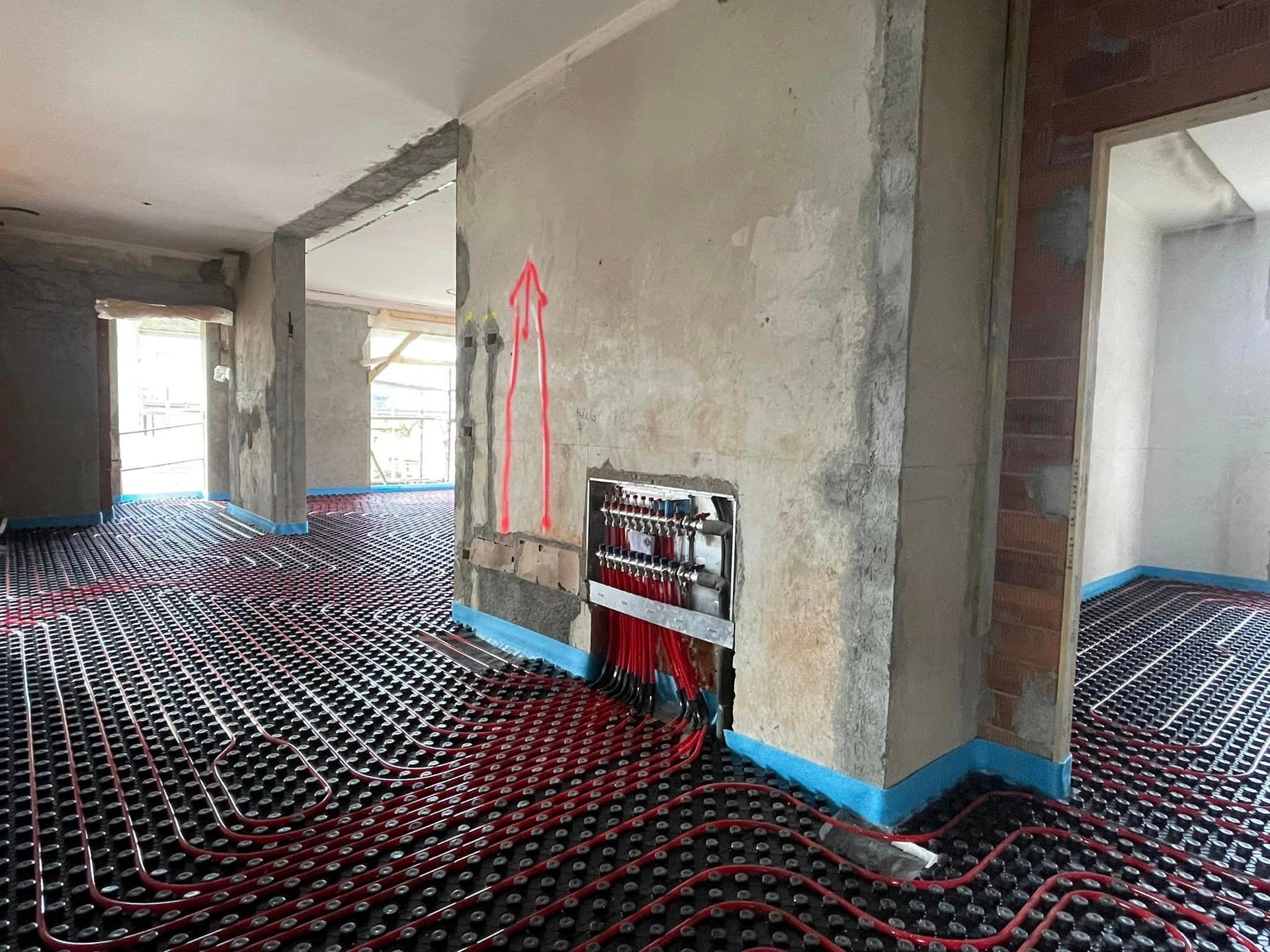 Interno in fase di ristrutturazione con sottofondo rosso sul pavimento, pareti non rifinite e nastro protettivo blu lungo i battiscopa.