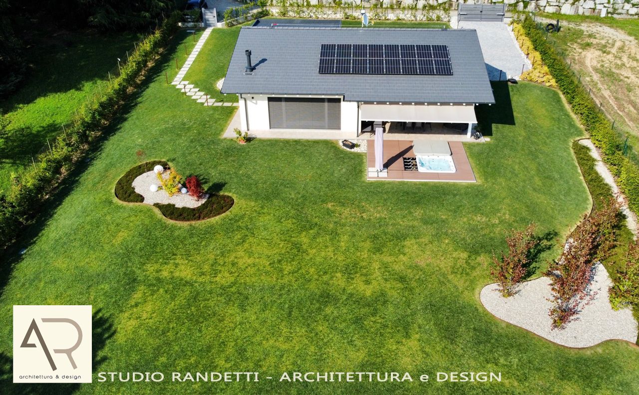 Veduta aerea di una casa moderna con pannelli solari, prato, patio e giardino paesaggistico.