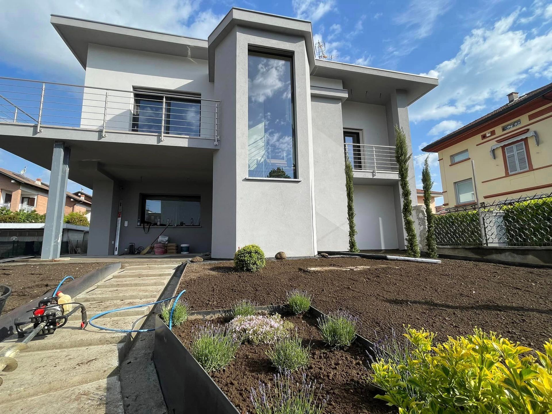 Casa moderna a due piani con balcone, vialetto d'accesso e giardino anteriore curato sotto un cielo azzurro.