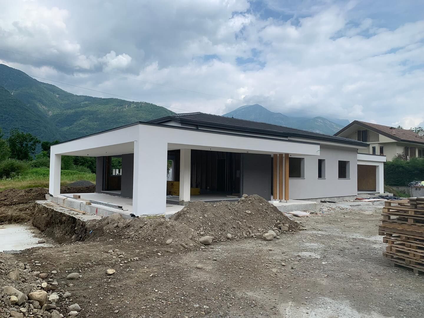 Casa moderna bianca in costruzione su un terreno roccioso con montagne sullo sfondo.