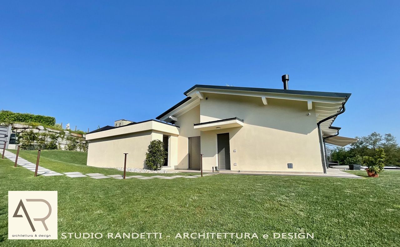 Casa moderna color beige con tetto spiovente su un pendio erboso sotto un cielo azzurro limpido
