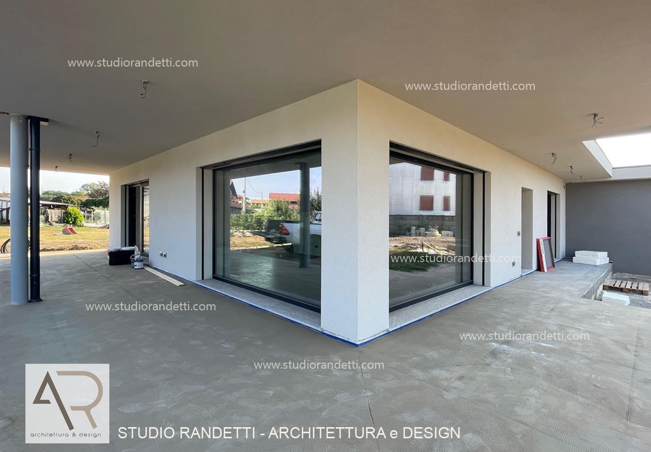 Esterno di una casa moderna con ampie finestre angolari, patio coperto e vialetto d'accesso in cemento.