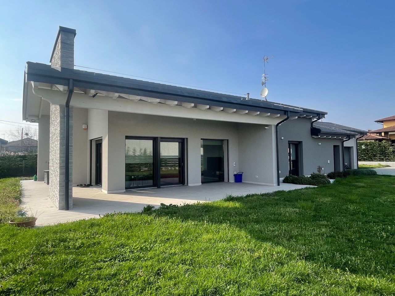 Casa moderna a un solo piano con esterni bianchi, tetto grigio, ampie finestre e giardino erboso.