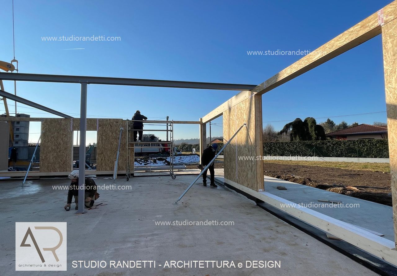 Struttura portante di una casa in costruzione con operai su una soletta di cemento in un cantiere aperto e soleggiato.