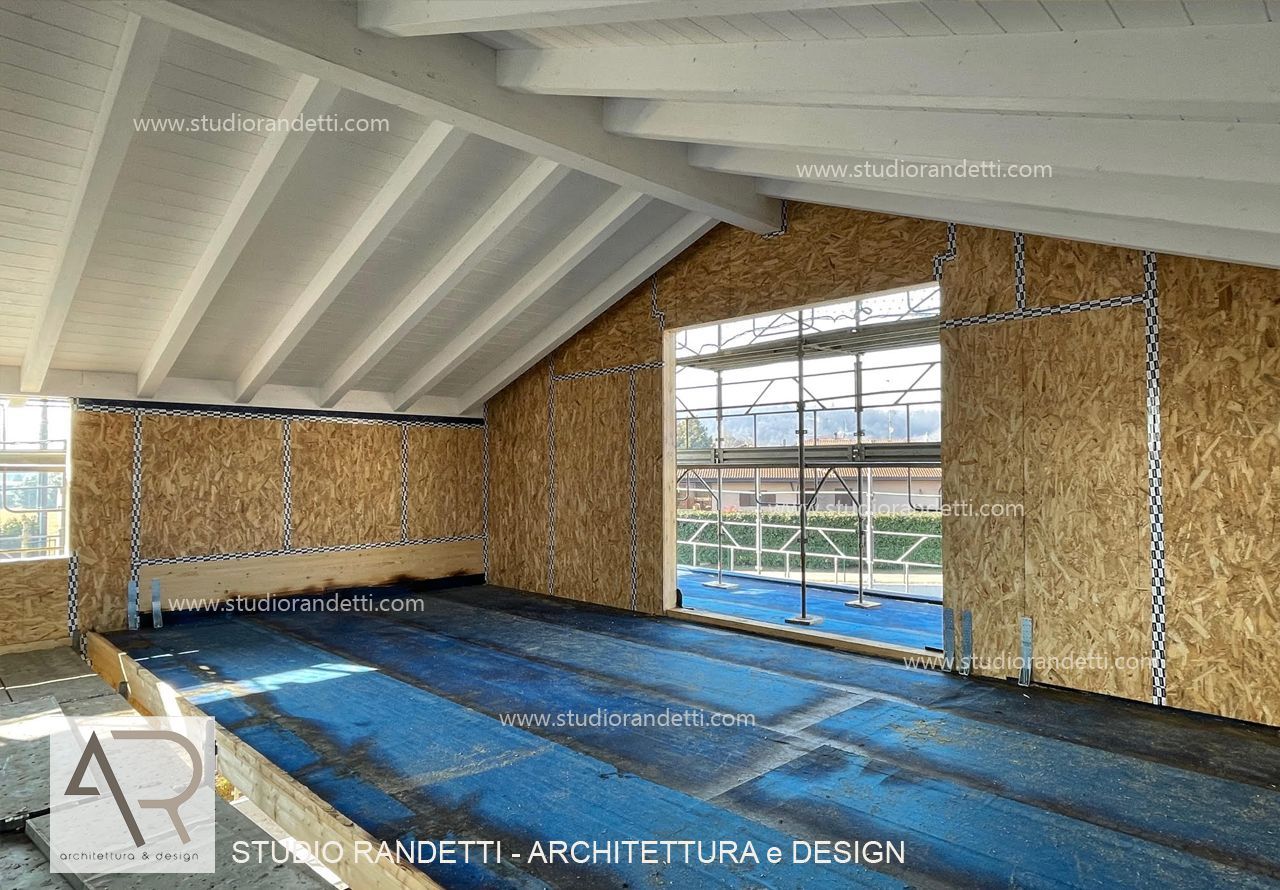 Locale di cantiere vuoto con pavimento blu, pareti in legno a vista e soffitto bianco inclinato con finestre.