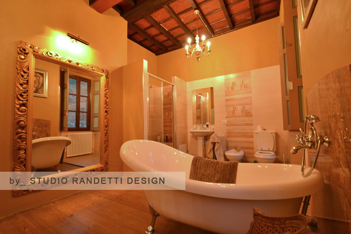 Bagno accogliente, illuminato da una luce ambrata, con vasca con piedini, doccia, mobile lavabo e soffitto con travi in ​​legno.