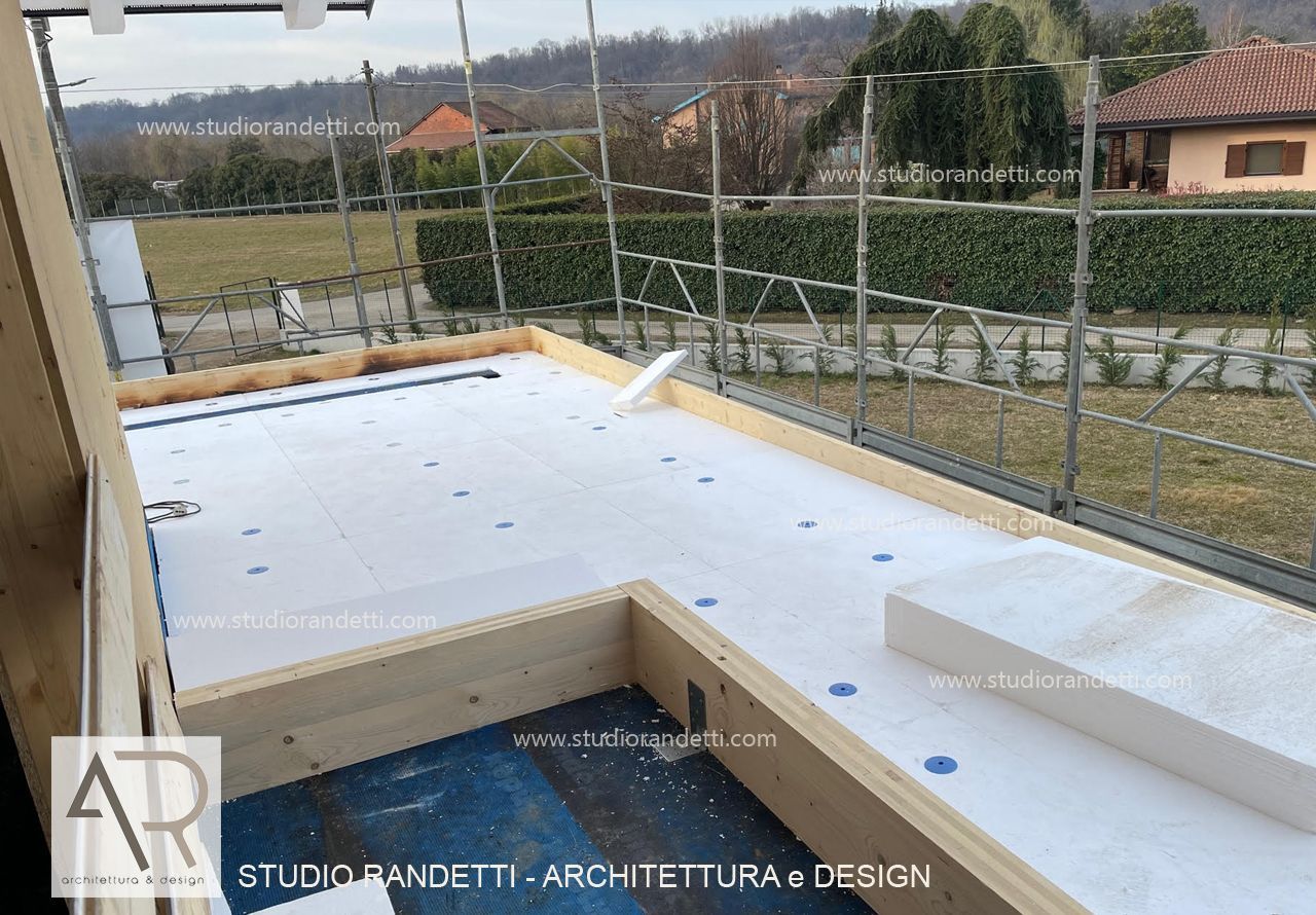 Terrazza con tetto piano in costruzione con membrana impermeabile bianca e vista sul cortile recintato.