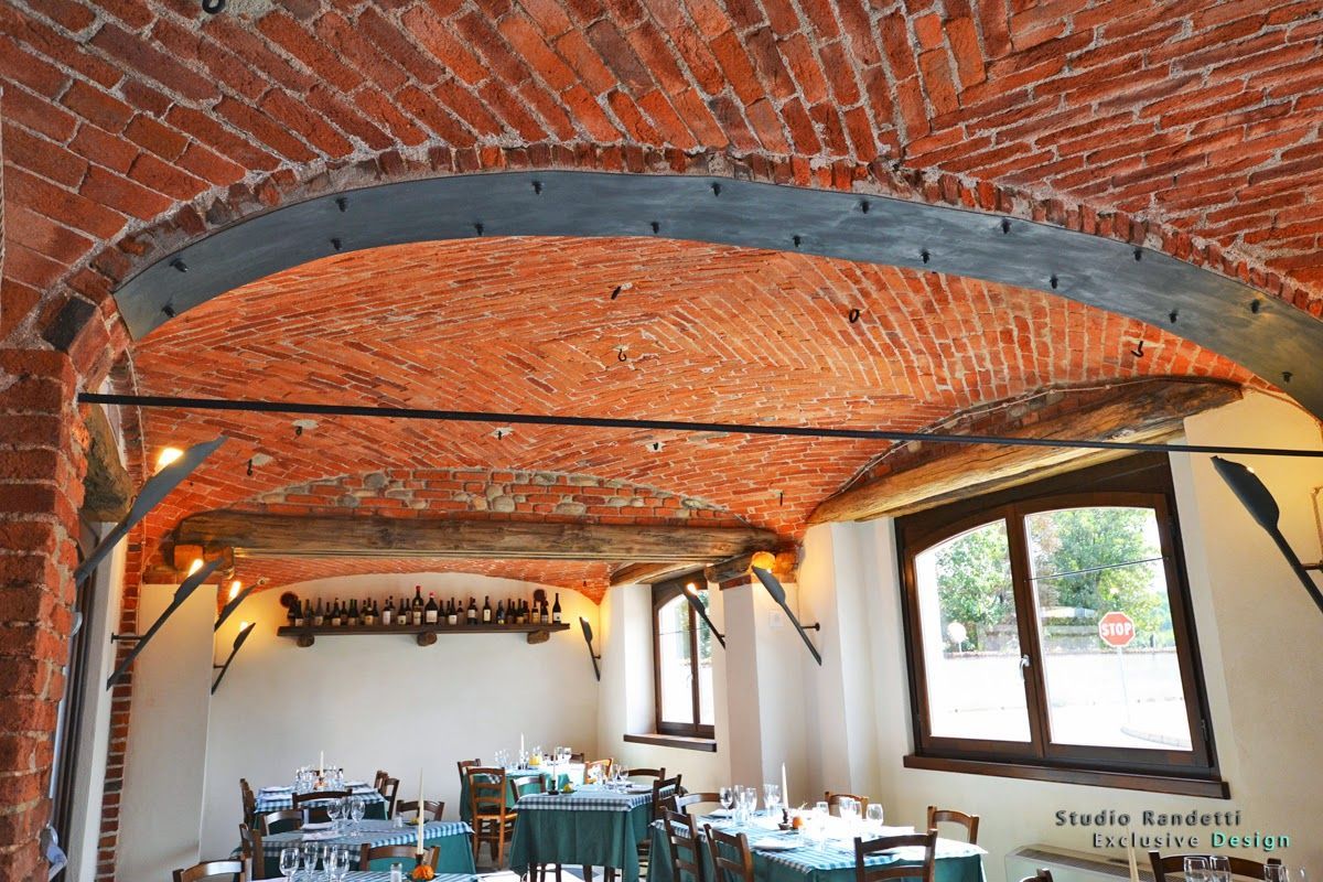 Sala da pranzo rustica con soffitto a volta in mattoni a vista, travi in ​​legno e tavoli disposti sotto le finestre.