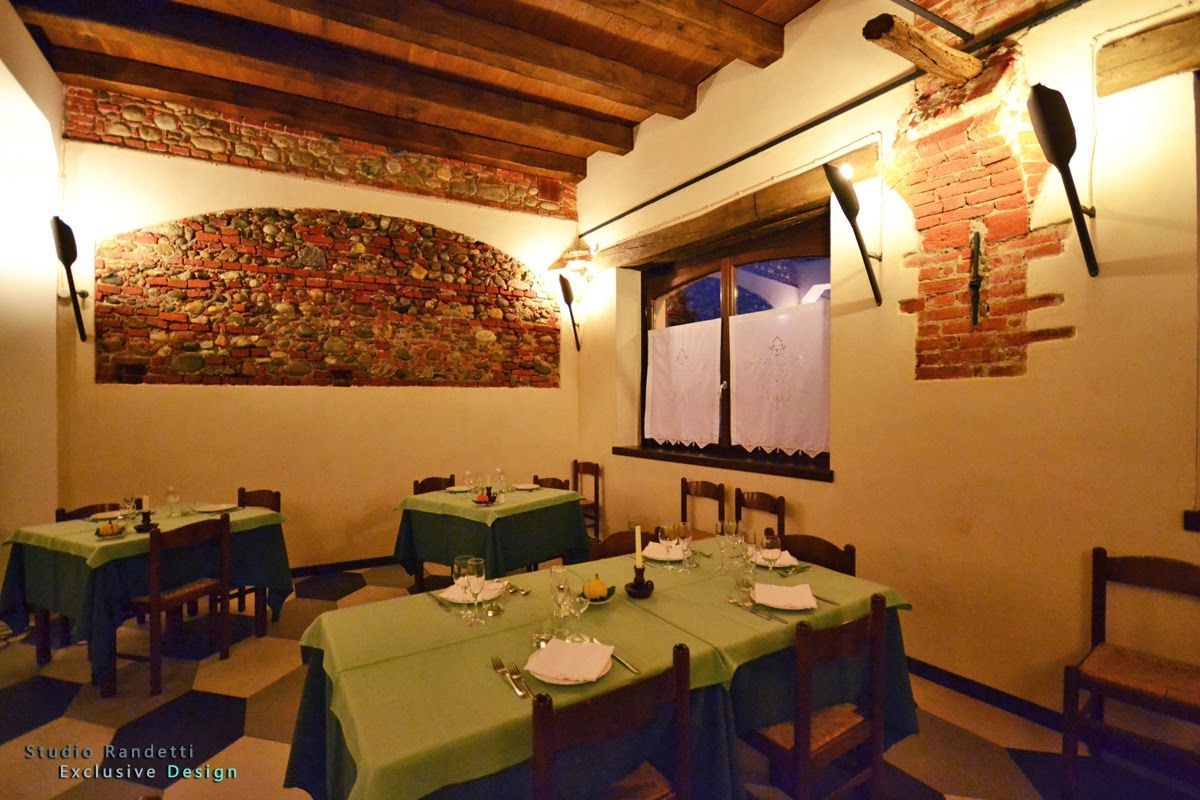 Accogliente sala da pranzo di un ristorante con tovaglie verdi, travi in ​​legno a vista, opere d'arte alle pareti e luci calde.