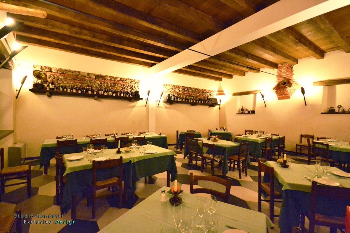 Sala da pranzo rustica e caldamente illuminata, con travi in ​​legno a vista, tovaglie bianche e tavoli e sedie disposti con cura.