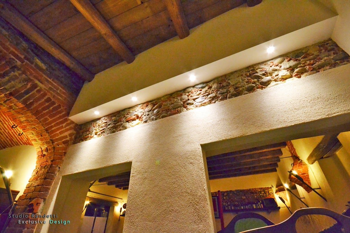 Interno rustico e caldo, illuminato da luci soffuse, con archi in mattoni, pareti con texture e travi in ​​legno sul soffitto.
