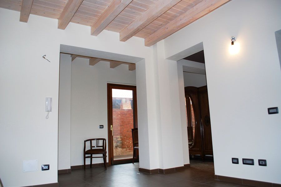 Stanza moderna vuota con pareti bianche, travi in ​​legno a vista e pavimento scuro, vista attraverso una porta.
