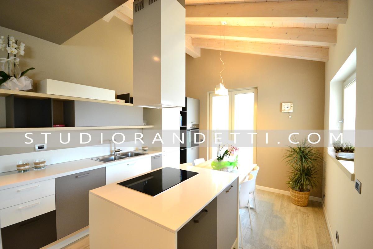 Cucina moderna e luminosa con mobili bianchi, travi in ​​legno, isola centrale e ampie finestre.