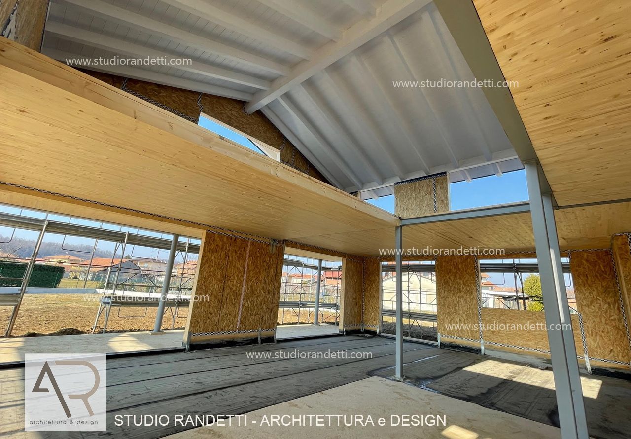 Interno di un moderno edificio in costruzione con struttura in legno, caratterizzato da travi a vista e ampie finestre.