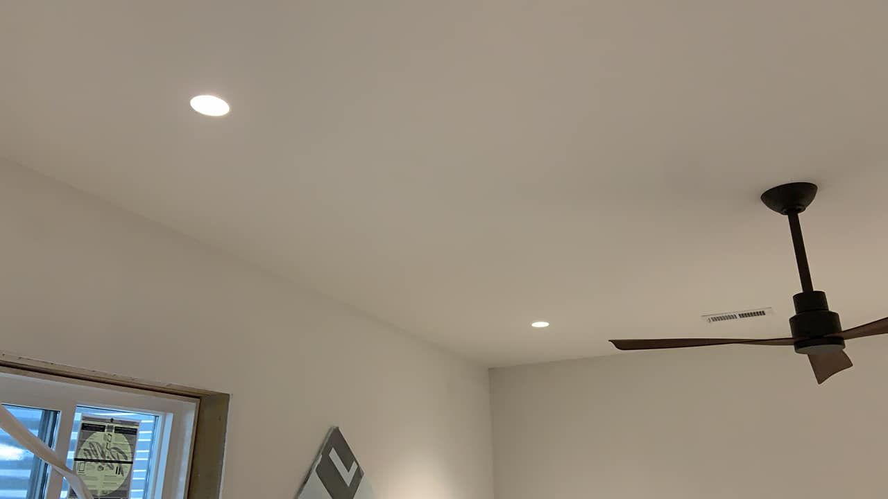 White ceiling with two recessed lights and a dark ceiling fan, beside a window.