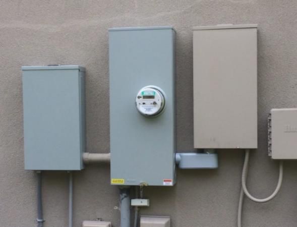 Outdoor electrical panel with meter, gray and beige boxes mounted on stucco wall.