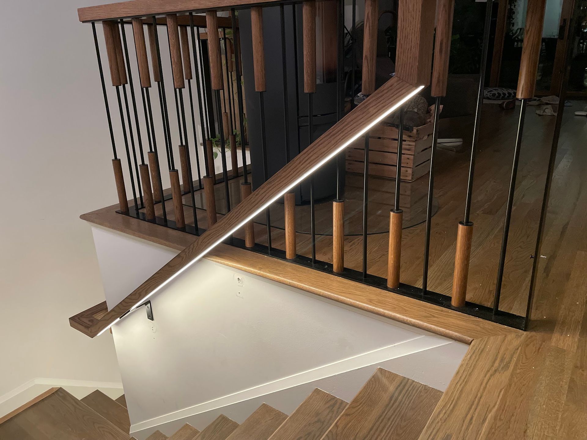 Staircase with wooden handrail, lit with strip lights. Black vertical bars between wood posts.