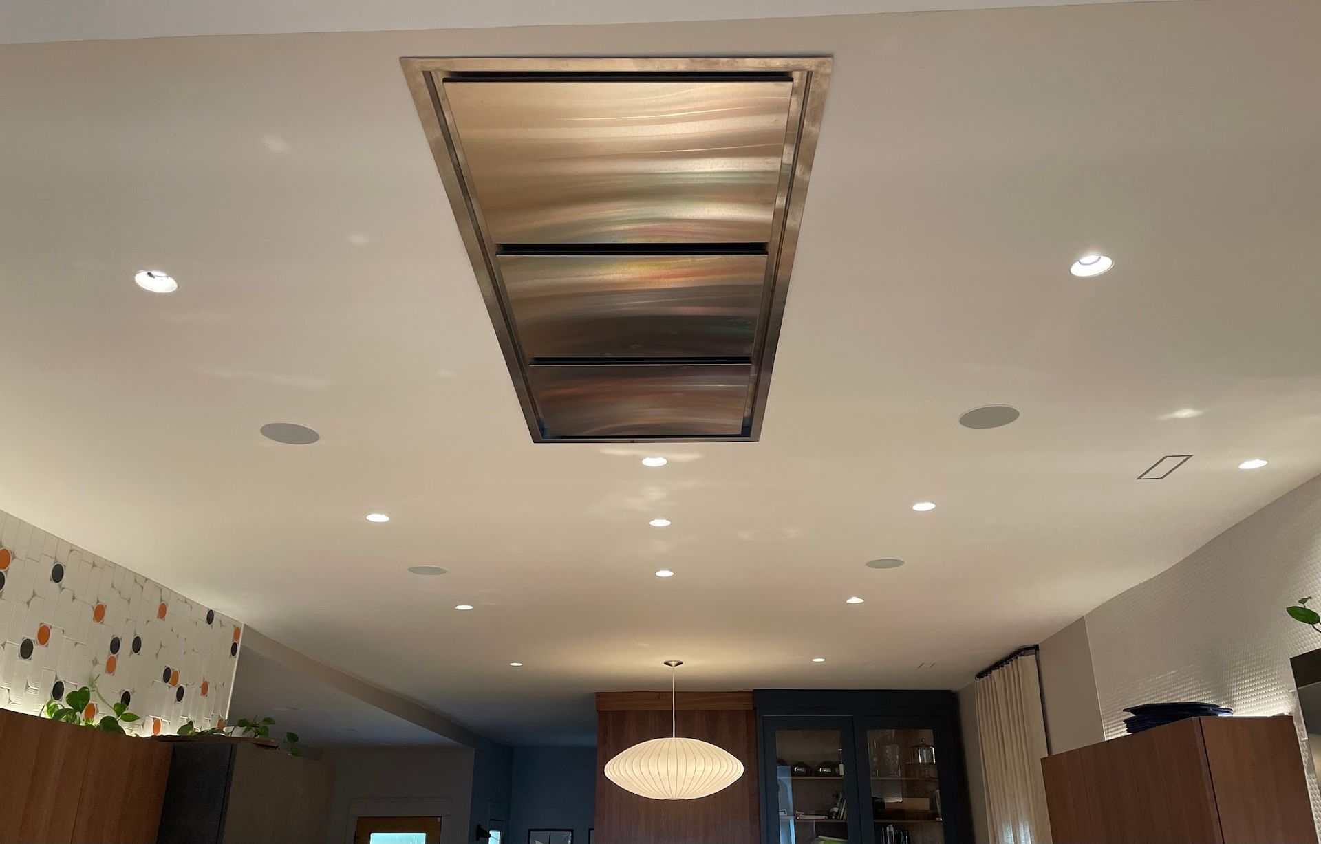 Stainless steel range hood centered on a white kitchen ceiling, surrounded by recessed lights.