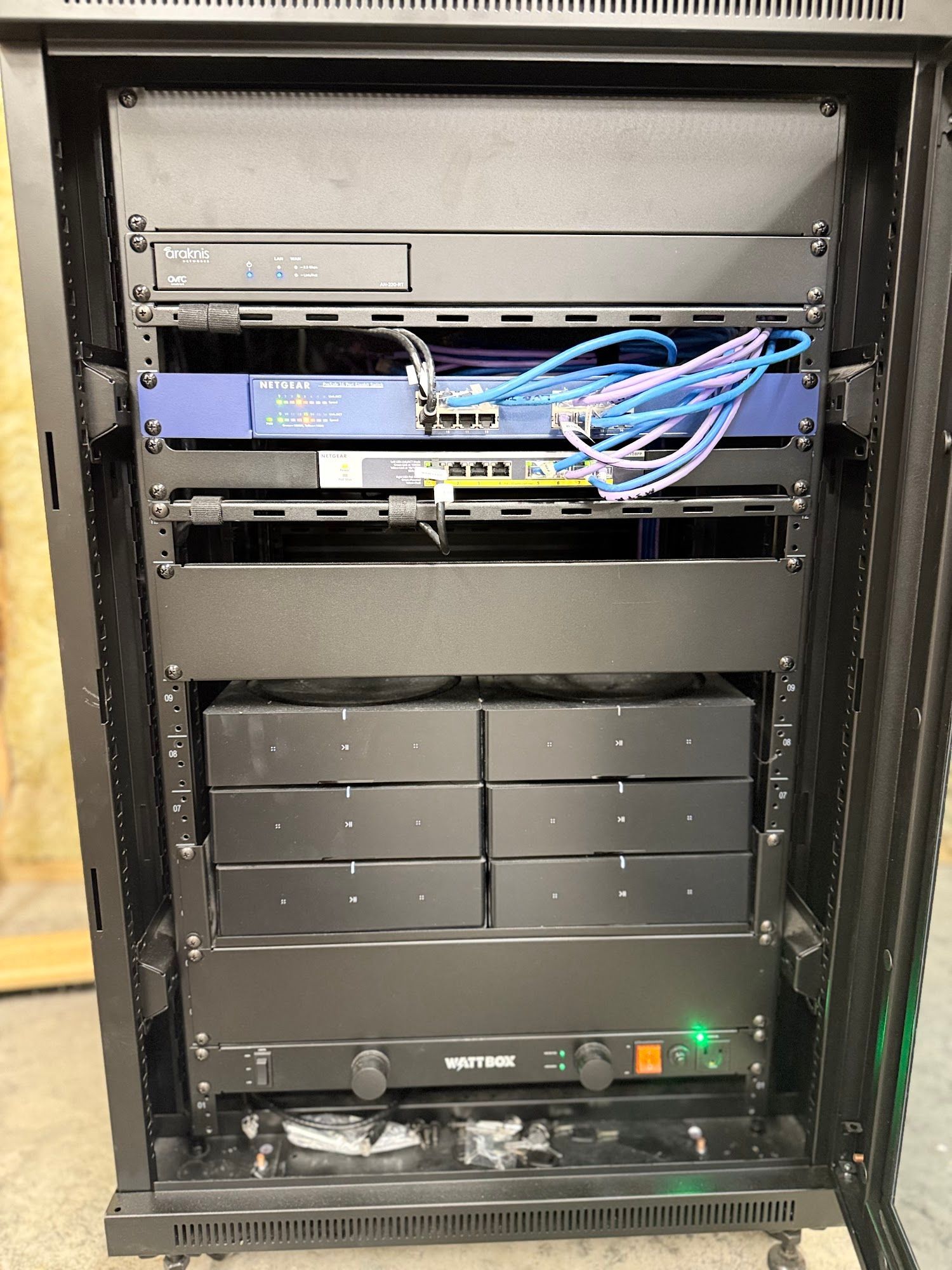 Black server rack filled with electronic equipment; blue cables are visible.
