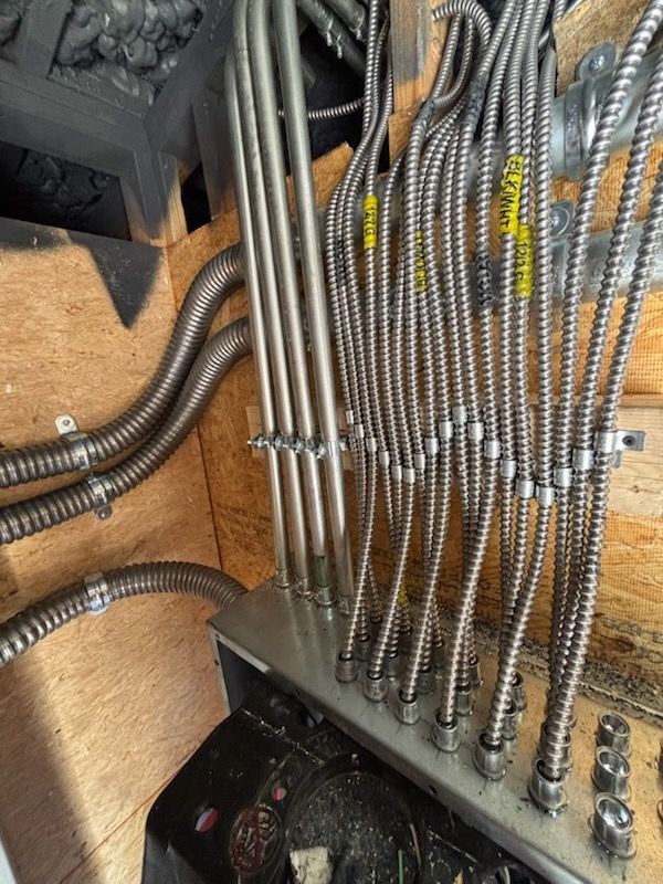 Electrical conduits and wires attached to a metal box on a wooden surface.