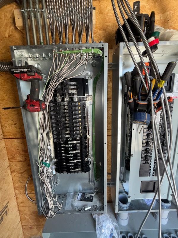 Two open electrical panels with wiring and circuit breakers, a red drill visible.
