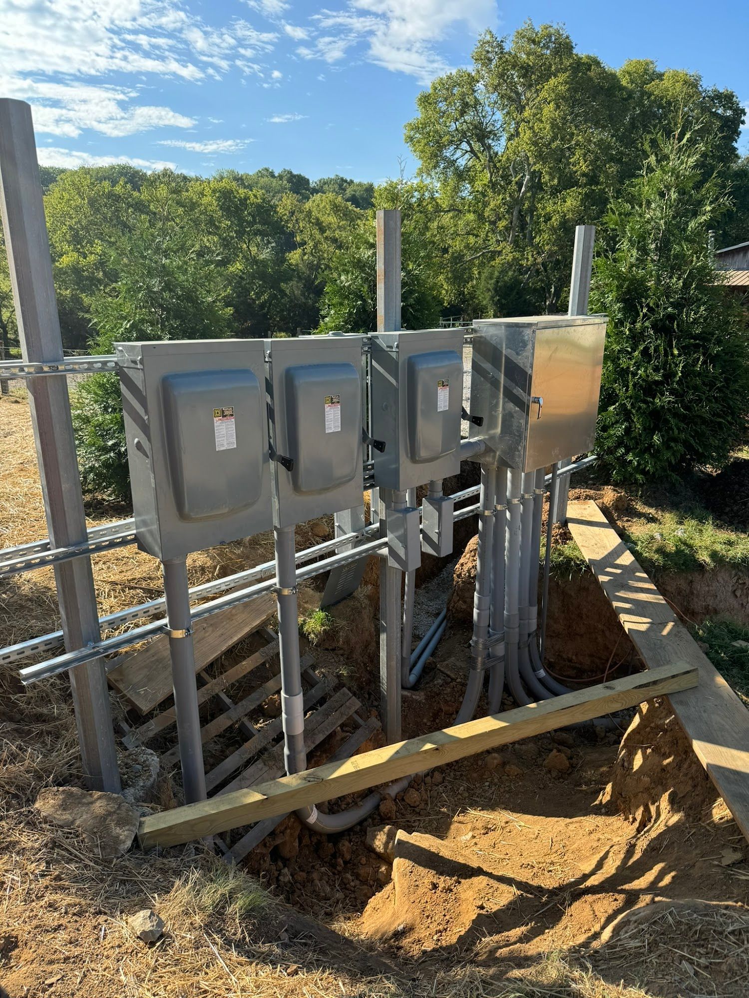 Electrical boxes and conduits installed outdoors, against a backdrop of trees and a blue sky.