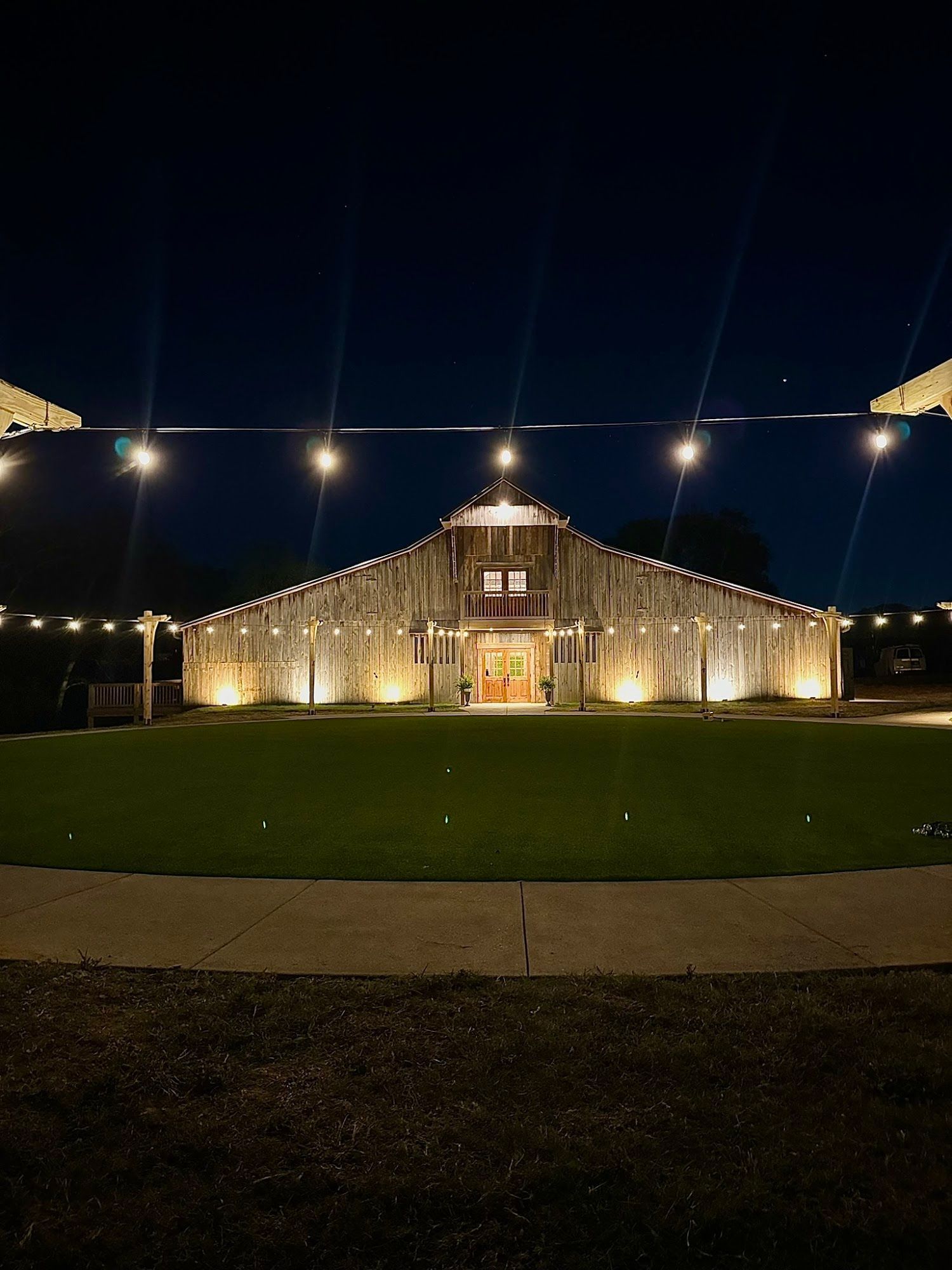 A rustic barn illuminated at night, with string lights overhead.