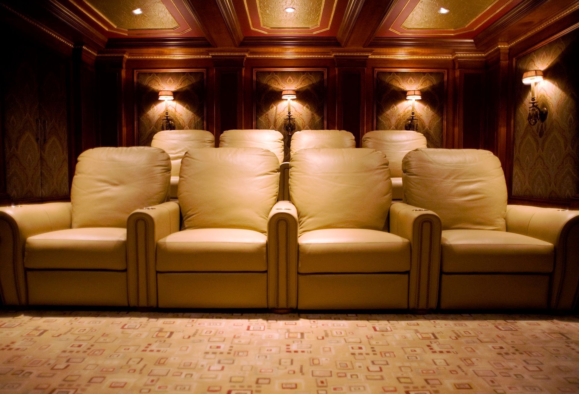 Home theater with beige leather recliners, wood paneling, and patterned carpet.