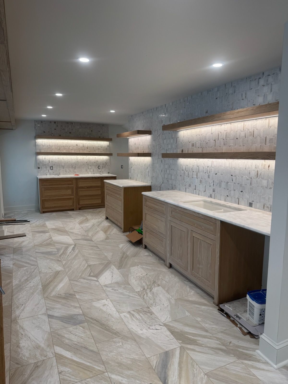 A partially finished kitchen with light-colored cabinets, marble countertops, and textured backsplash.