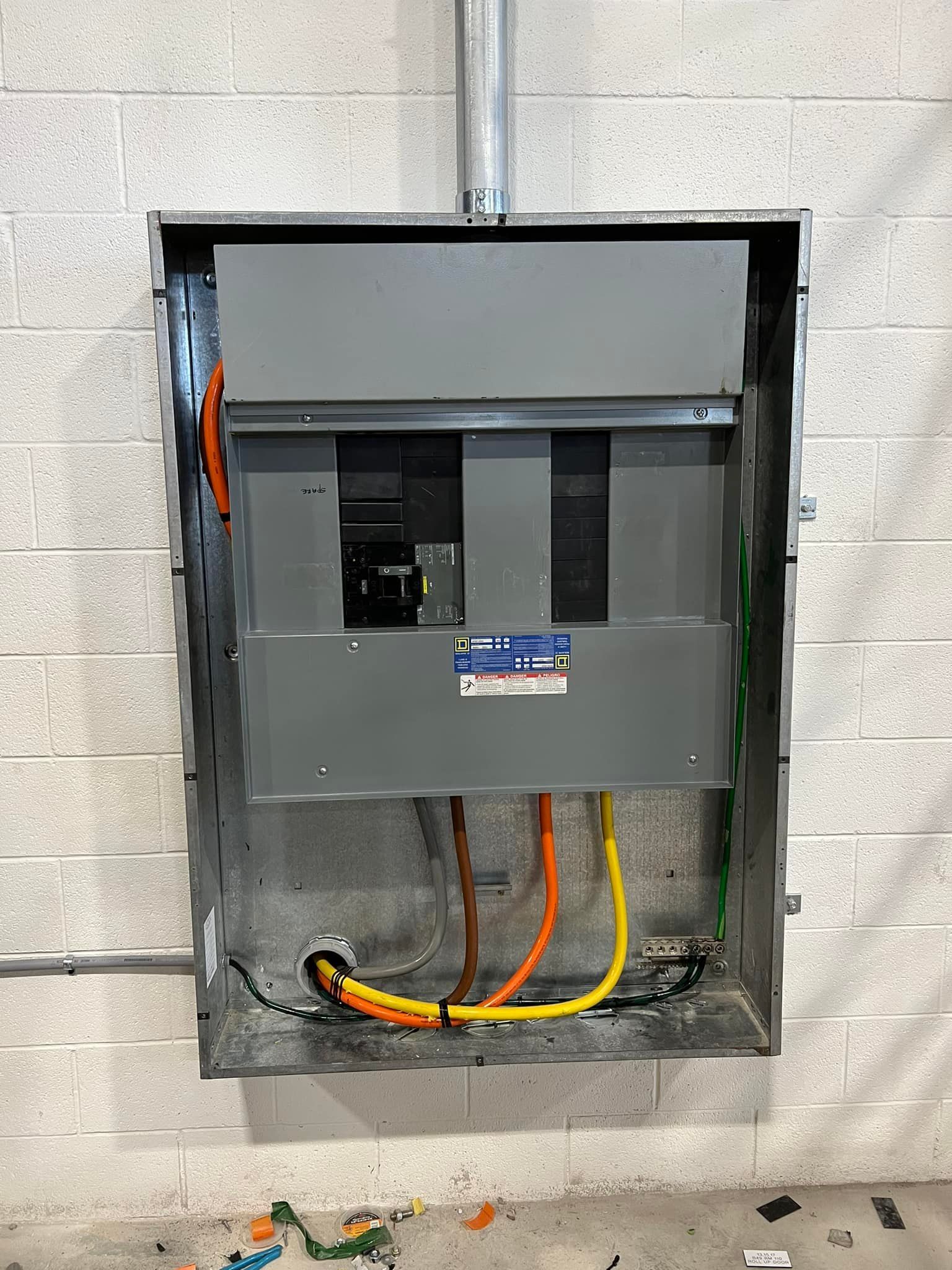 Electrical panel mounted in a metal box on a cinder block wall; orange, yellow, and brown wires are visible.