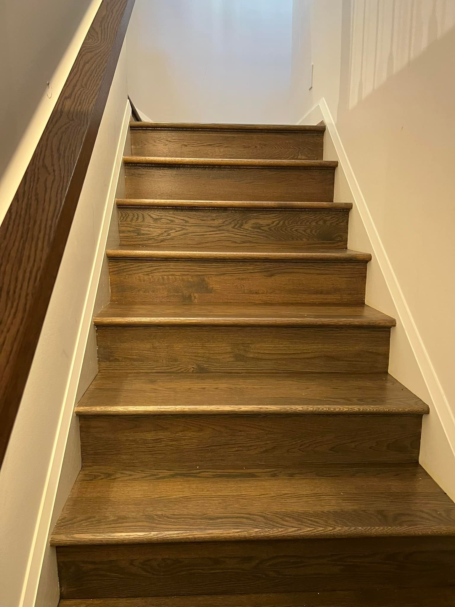Wooden staircase with a dark brown handrail on the left side, ascending.
