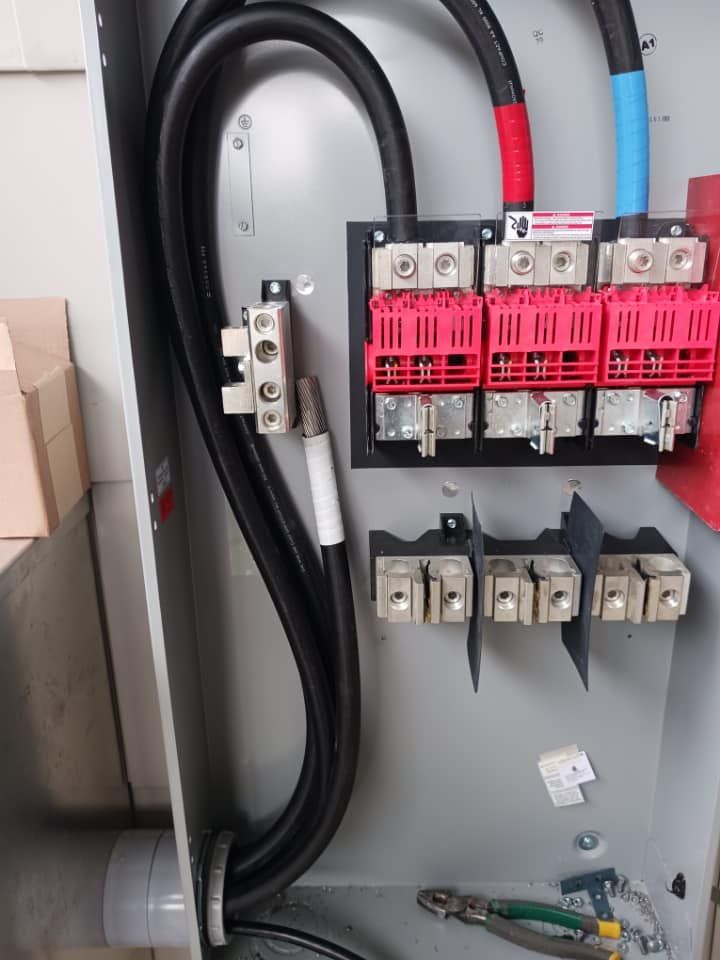 Electrical panel with black cables connected to red and white terminals. Green grounding wire.