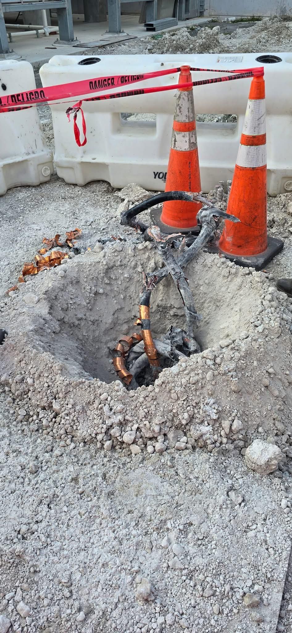 Open hole in the ground, construction site with cones and caution tape.