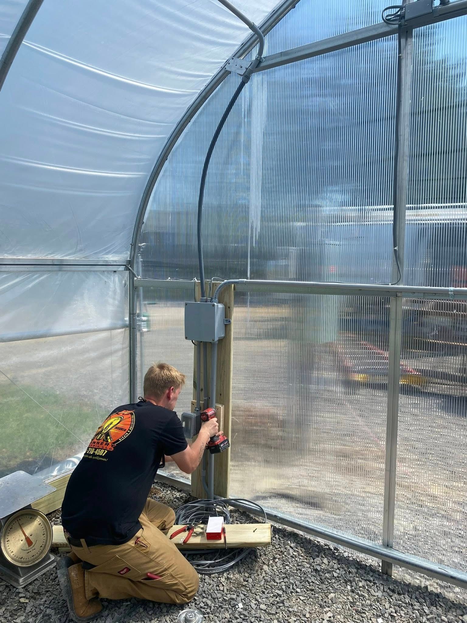 Person installing electrical box inside a greenhouse.