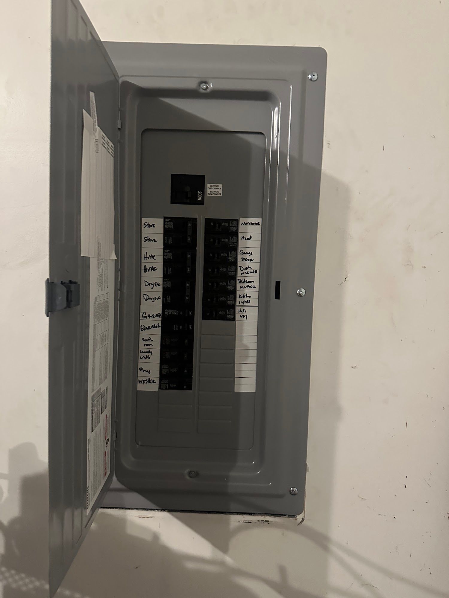Gray electrical circuit breaker box mounted on a white wall, door open.