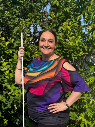Gina smiling holding her cane with trees in the background